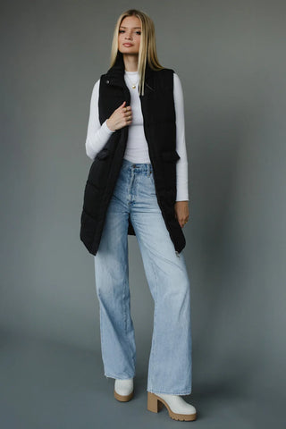 Woman wearing a black vest, white shirt, light blue jeans, and white shoes on a gray background – JSQ Mercantile Women’s Boutique & Gift Shop Located in La Grange, IL